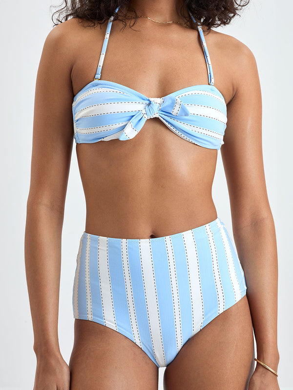 Close up on a Woman wearing  lemlem ELSI High Waist bottom and AVA Bandeau Top featuring bold, crisp white stripes on a sky-blue background, accented with black detailing.