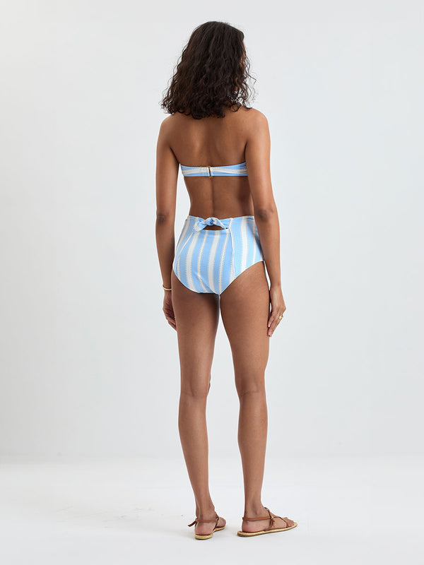 Back of a Woman wearing  lemlem ELSI High Waist bottom and AVA Bandeau Top featuring bold, crisp white stripes on a sky-blue background, accented with black detailing.