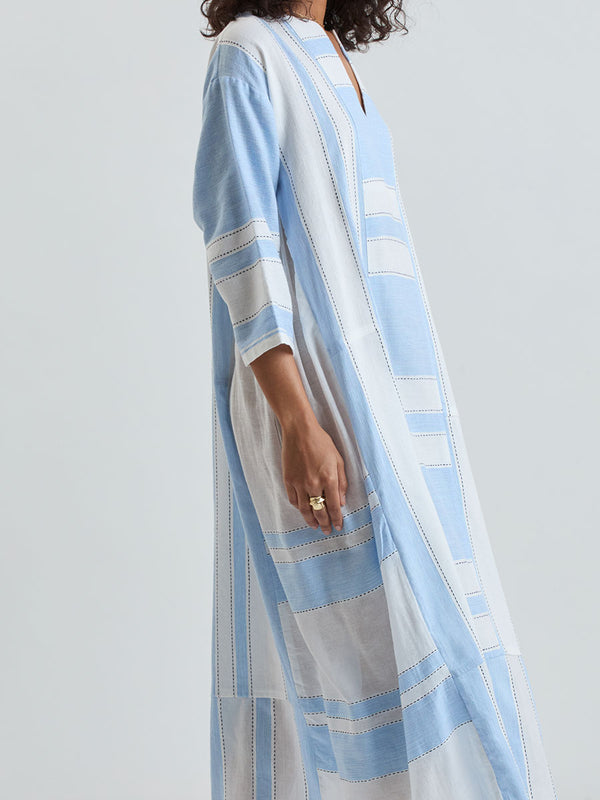Close up on a Woman wearing a lemlem  handwoven FANA Caftan  featuring bold, crisp white stripes on a sky-blue background, accented with black stitch detailing