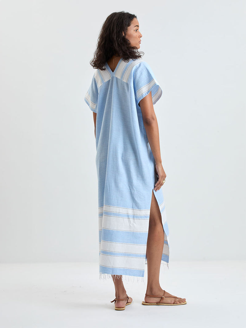 Back of a woman wearing lemlem GASIRA Caftan featuring color block stripe pattern in white on sky blue background
