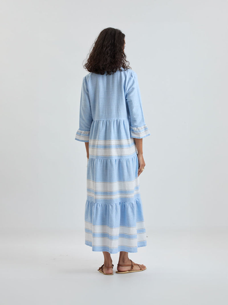 Back of a Woman wearing lemlem handwoven HAWI Dress featuring bold, crisp white stripes on a sky-blue background, accented with black stitch detailing