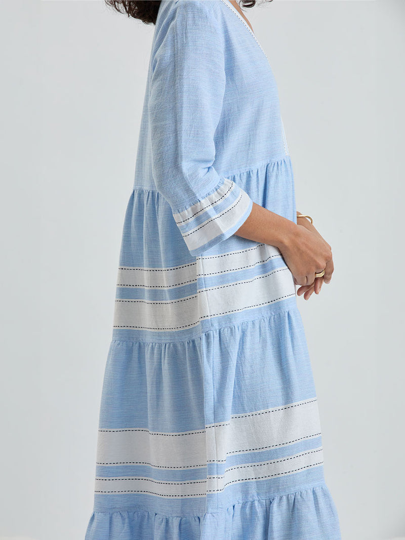 Close up on a Woman wearing lemlem handwoven HAWI Dress featuring bold, crisp white stripes on a sky-blue background, accented with black stitch detailing