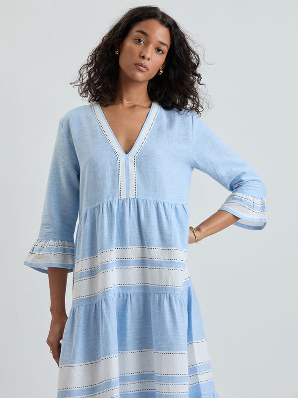 Woman wearing lemlem handwoven HAWI Dress featuring bold, crisp white stripes on a sky-blue background, accented with black stitch detailing