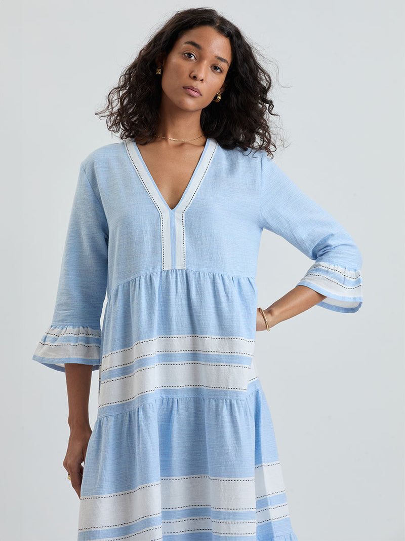 Woman wearing lemlem handwoven HAWI Dress featuring bold, crisp white stripes on a sky-blue background, accented with black stitch detailing