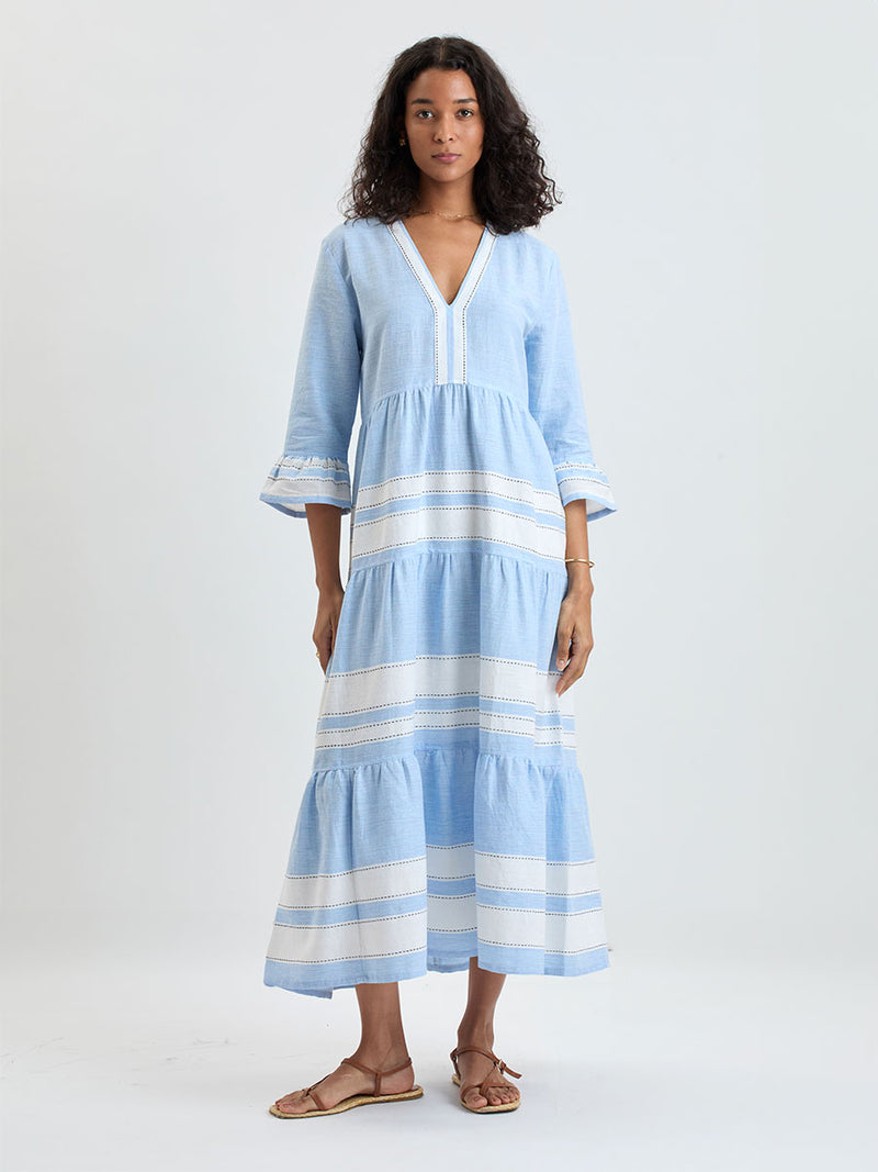 Woman wearing lemlem handwoven HAWI Dress featuring bold, crisp white stripes on a sky-blue background, accented with black stitch detailing