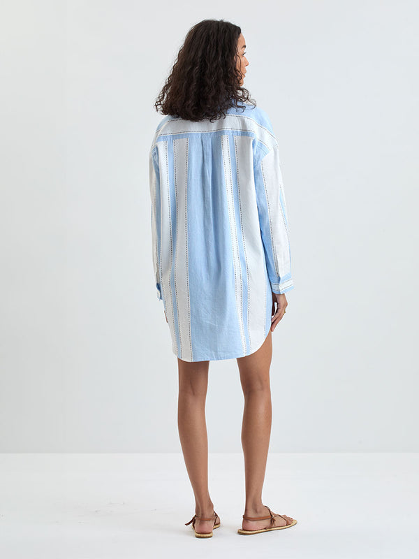 Back of a Woman Standing wearing lemlem MARIAM Handwoven shirt featuring bold, crisp white stripes on a sky-blue background, accented with black stitch detailing
