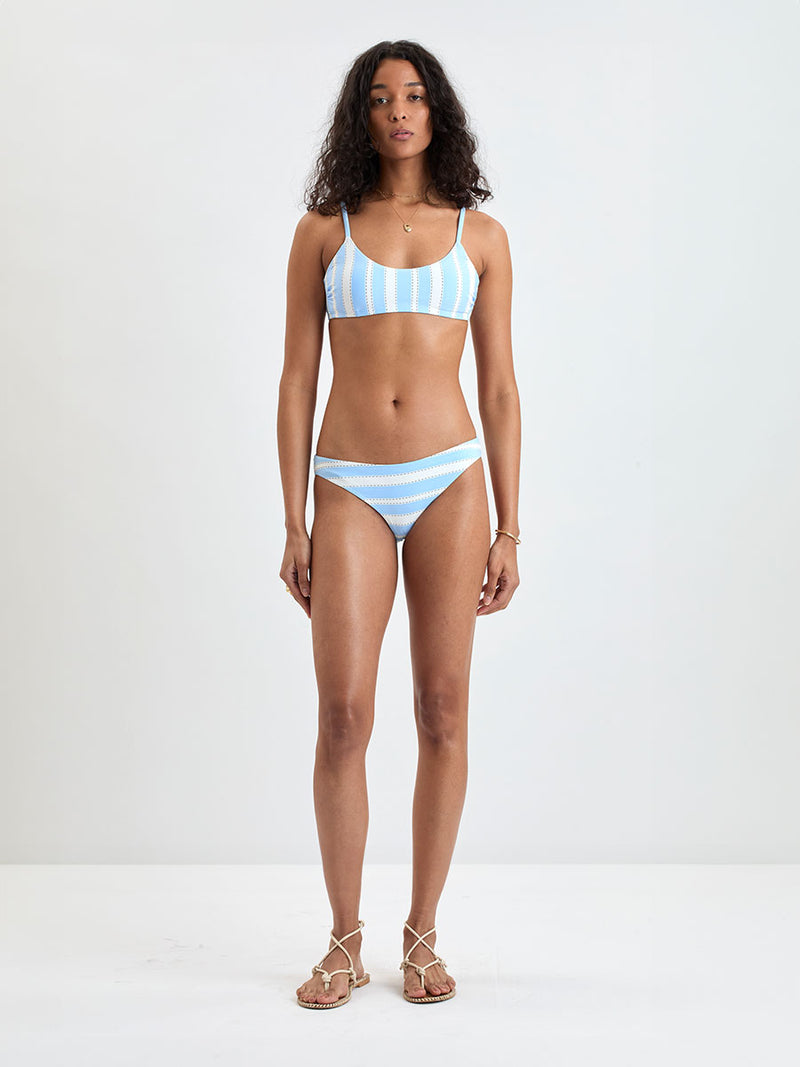 Woman wearing  lemlem ASHA Scoop Top and MERON Birief Bottom featuring bold, crisp white stripes on a sky-blue background, accented with black detailing.