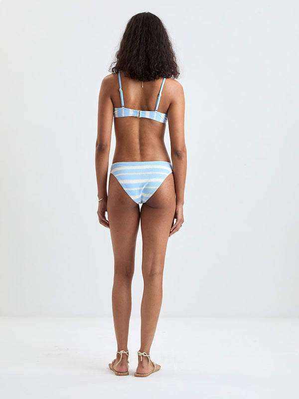 Back of a Woman wearing  lemlem ASHA Scoop Top and MERON Birief Bottom featuring bold, crisp white stripes on a sky-blue background, accented with black detailing.