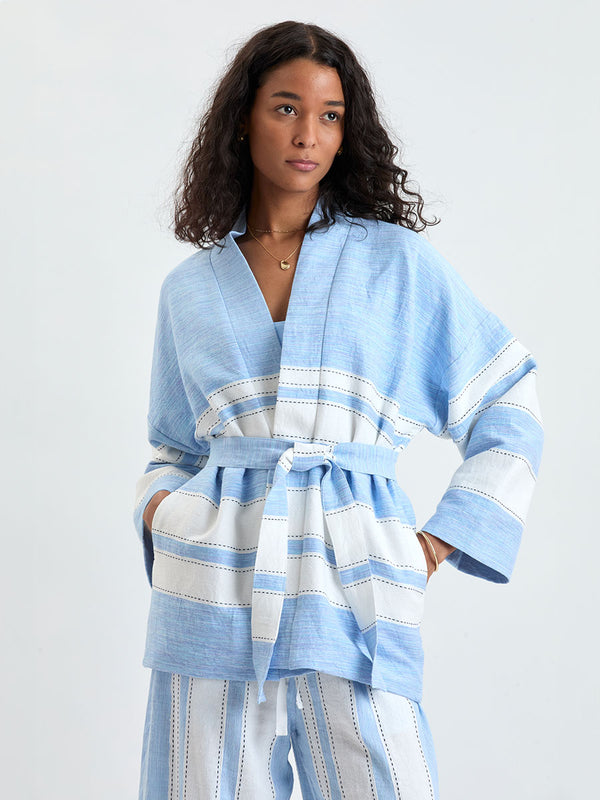 Woman Standing wearing lemlem TERARA Jacket and DESTA Pants featuring bold, crisp white stripes on a sky-blue background, accented with black detailing.