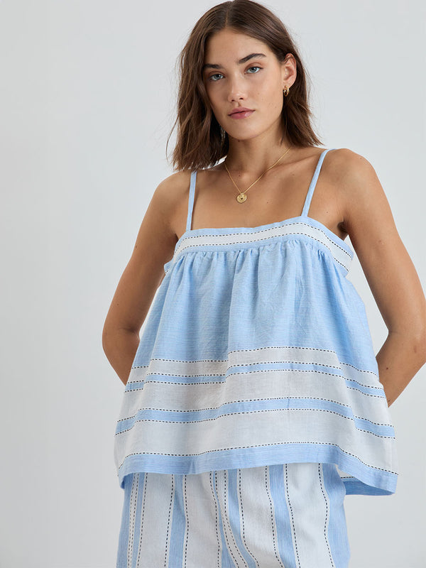 Woman standing wearing lemlem handwoven THEA Tank Top featuring bold, crisp white stripes on a sky-blue background, accented with black stitch detailing