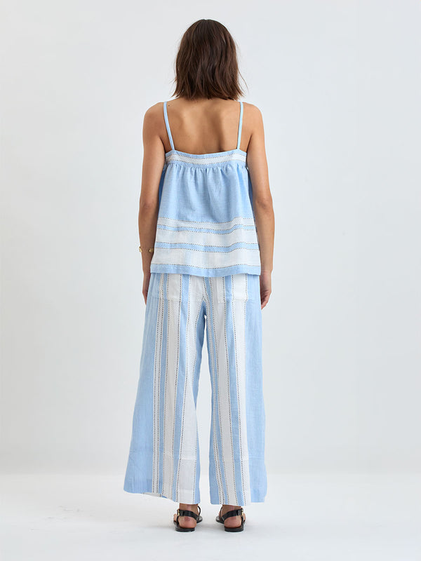 Bacl of a Woman standing wearing lemlem handwoven THEA Tank Top featuring bold, crisp white stripes on a sky-blue background, accented with black stitch detailing