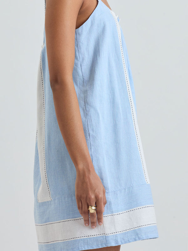 Close up on a Woman Standing wearing lemlem ZINA Dress featuring bold, crisp white stripes on a sky-blue background, accented with black detailing.