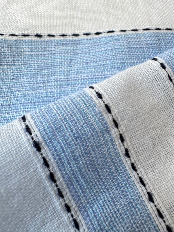 Close up on lemlem fabric featuring bold, crisp white stripes on a sky-blue background, accented with black stitch detailing