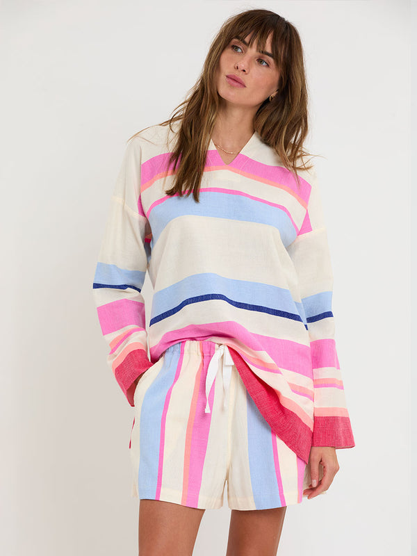 Woman standing wearing lemlem handwoven HENOK Hoodie and SAFIA Shorts featuring bold color block stripe pattern in pink, peach, red, sky and marine colors on vanilla background.