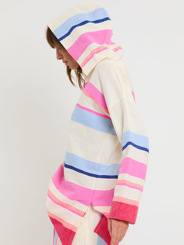 Woman standing wearing lemlem handwoven HENOK Hoodie and SAFIA Shorts featuring bold color block stripe pattern in pink, peach, red, sky and marine colors on vanilla background.