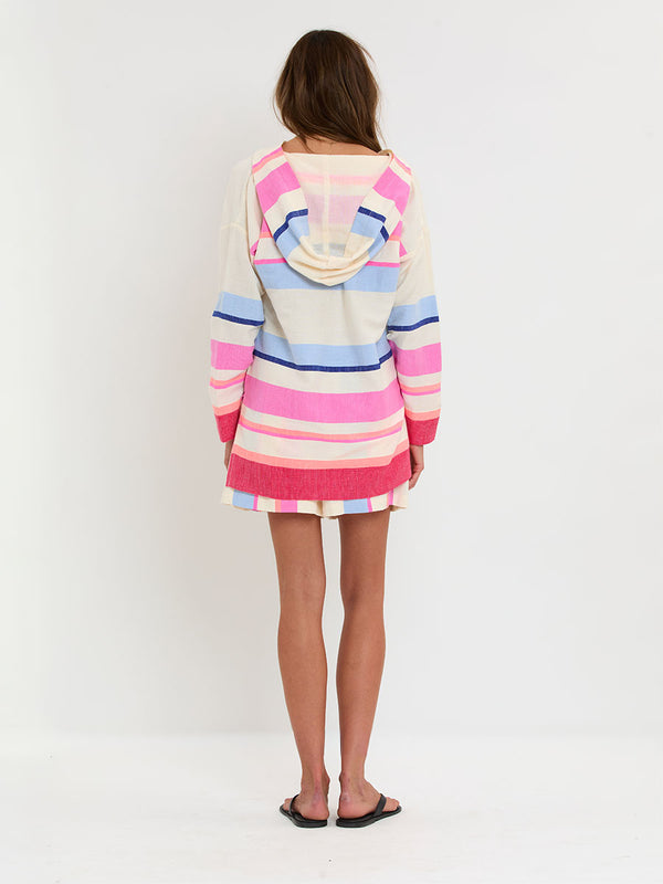 Woman standing wearing lemlem handwoven HENOK Hoodie and SAFIA Shorts featuring bold color block stripe pattern in pink, peach, red, sky and marine colors on vanilla background.