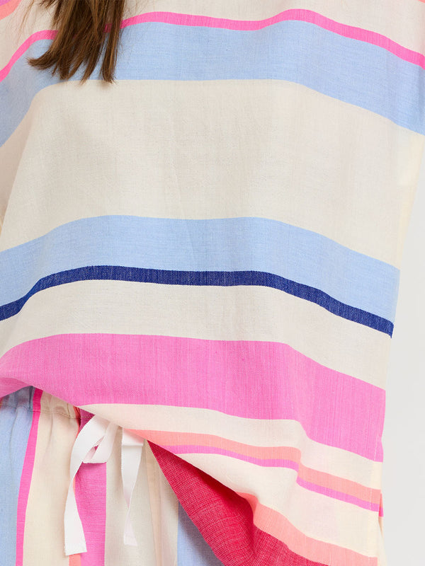 Woman standing wearing lemlem handwoven HENOK Hoodie and SAFIA Shorts featuring bold color block stripe pattern in pink, peach, red, sky and marine colors on vanilla background.