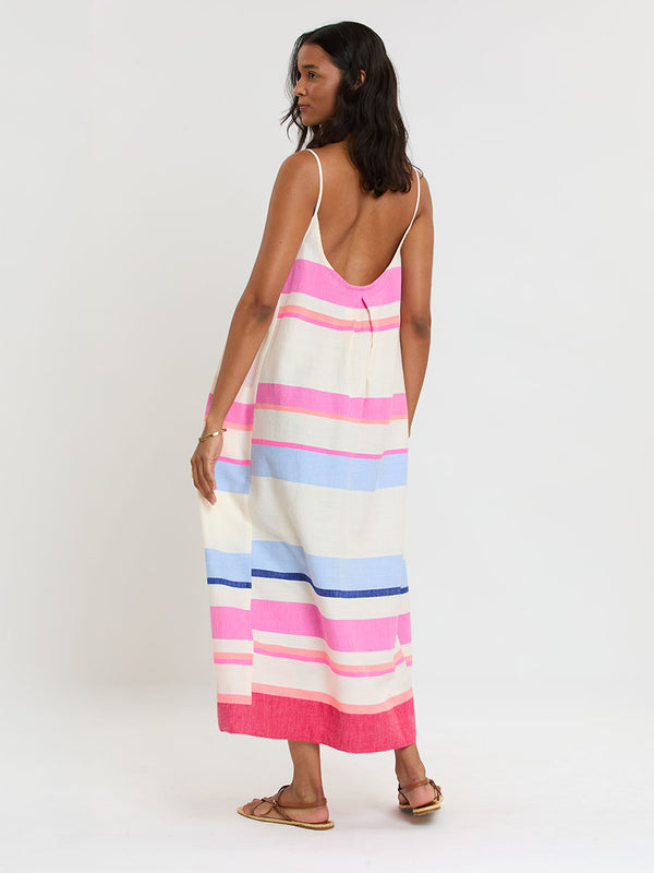 Woman standing wearing lemlem handwoven NIA Slip Dress featuring bold color block stripe pattern in pink, peach, red, sky and marine colors on vanilla background.