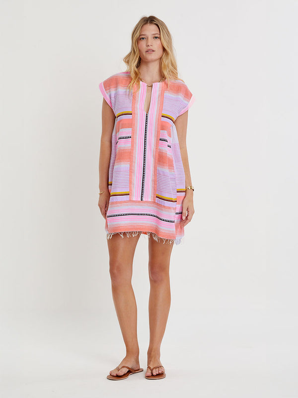 Woman standing wearing lemlem handwoven  ELINA Caftan featuring intricate stripe pattern interlaced with delicate mini Tibeb detailing, expressed in a soft yet vivid palette of cool pink, warm tangerine, rose, orchid, and accents of peach and deep burgundy.