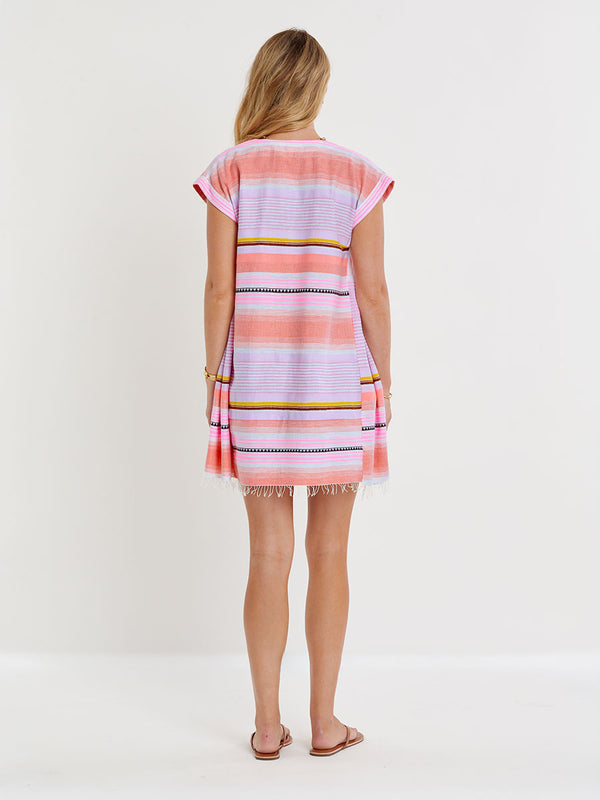Woman standing wearing lemlem handwoven ELINA Caftan featuring intricate stripe pattern interlaced with delicate mini Tibeb detailing, expressed in a soft yet vivid palette of cool pink, warm tangerine, rose, orchid, and accents of peach and deep burgundy.