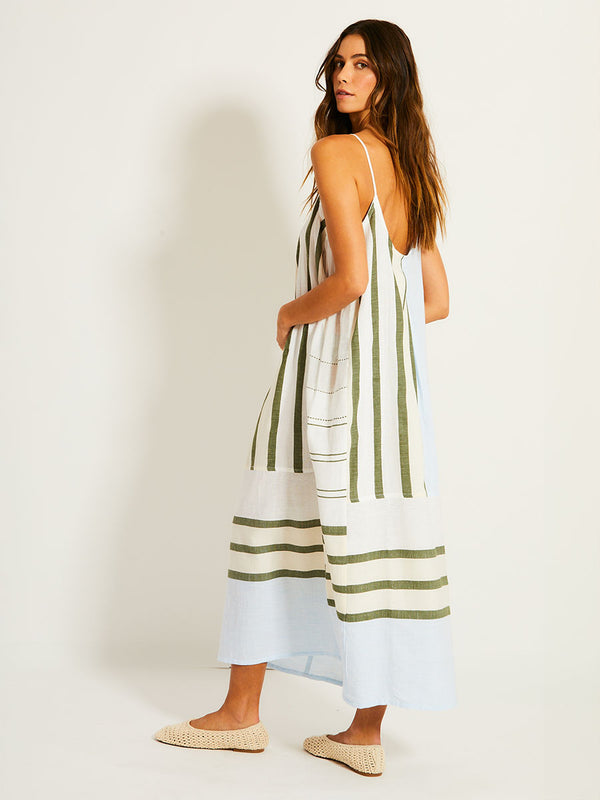Side Shot of Woman Standing Wearing lemlem NIA Dress featuring a bold asymmetrical color-block pattern, where airy light blue effortlessly blends with soft sage and cream