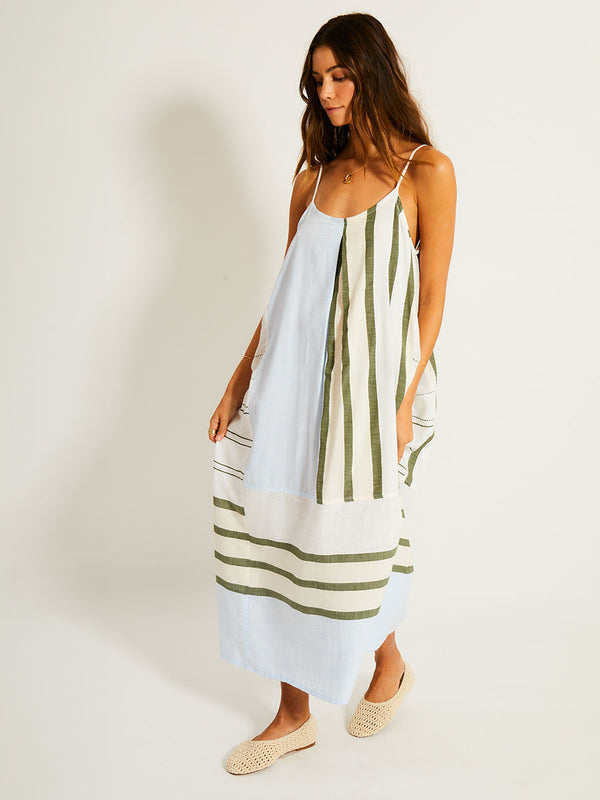 Woman Walking Wearing lemlem NIA Dress featuring a bold asymmetrical color-block pattern, where airy light blue effortlessly blends with soft sage and cream