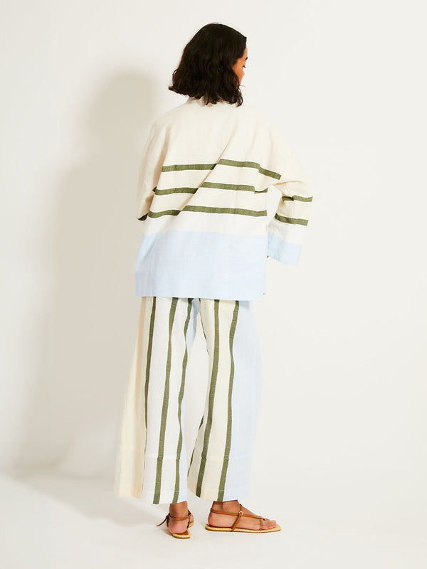 Back of a Woman Standing Wearing lemlem TERARA Jacket featuring a bold asymmetrical color-block pattern, where airy light blue effortlessly blends with soft sage and cream