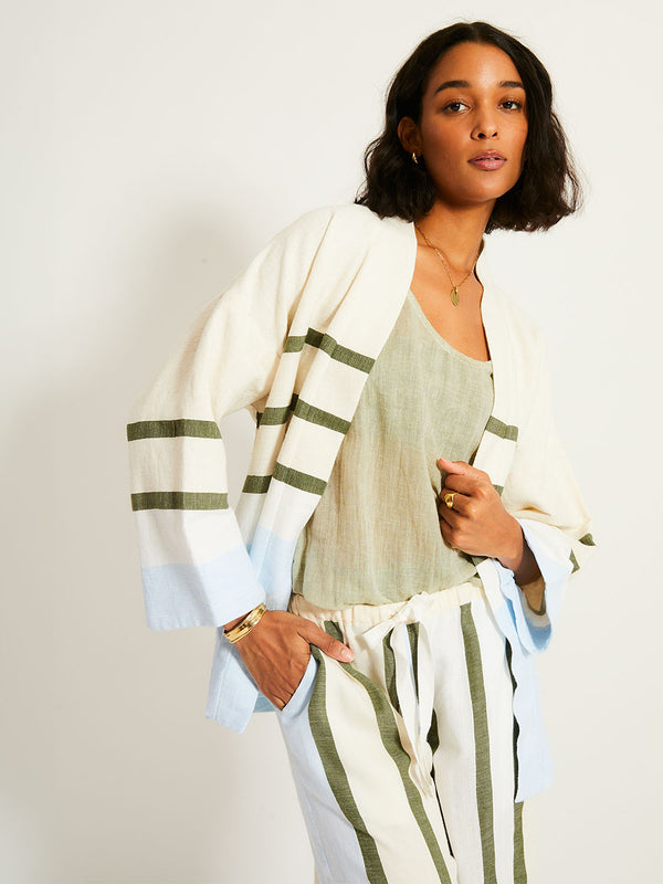 Woman Standing Wearing lemlem TERARA Jacket featuring a bold asymmetrical color-block pattern, where airy light blue effortlessly blends with soft sage and cream