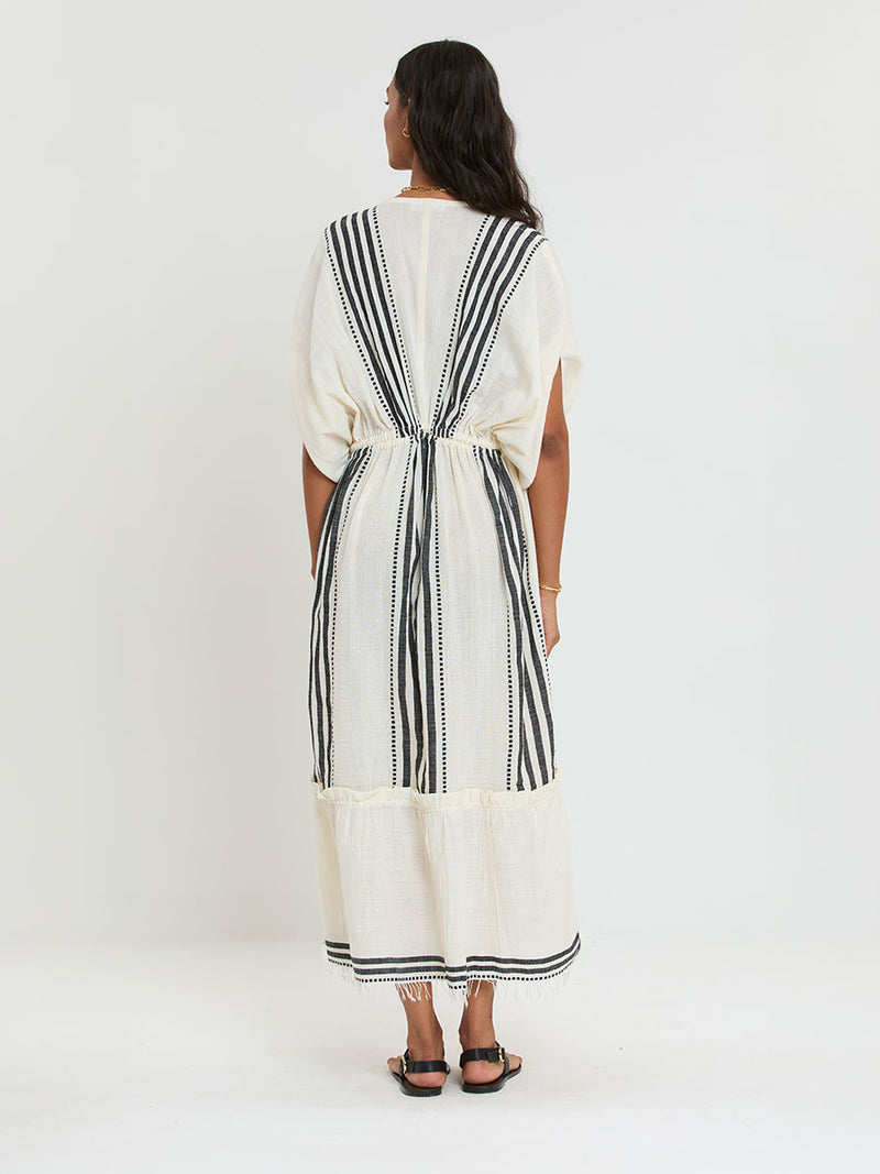 Back of a Woman Standing Wearing lemlem LEILA Plunge Dress featuring striped and dotted pattern in black color on cream background