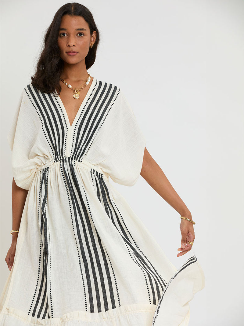 Woman Standing Wearing lemlem LEILA Plunge Dress featuring striped and dotted pattern in black color on cream background