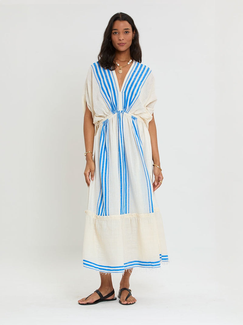 Woman Standing Wearing lemlem LEILA Plunge Dress featuring striped pattern in blue color on cream background