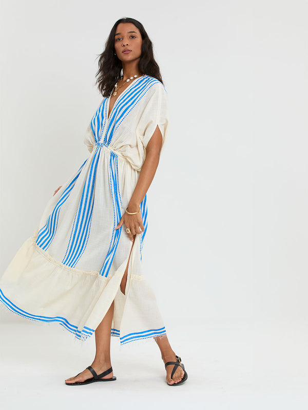 Woman Standing Wearing lemlem LEILA Plunge Dress featuring striped pattern in blue color on cream background