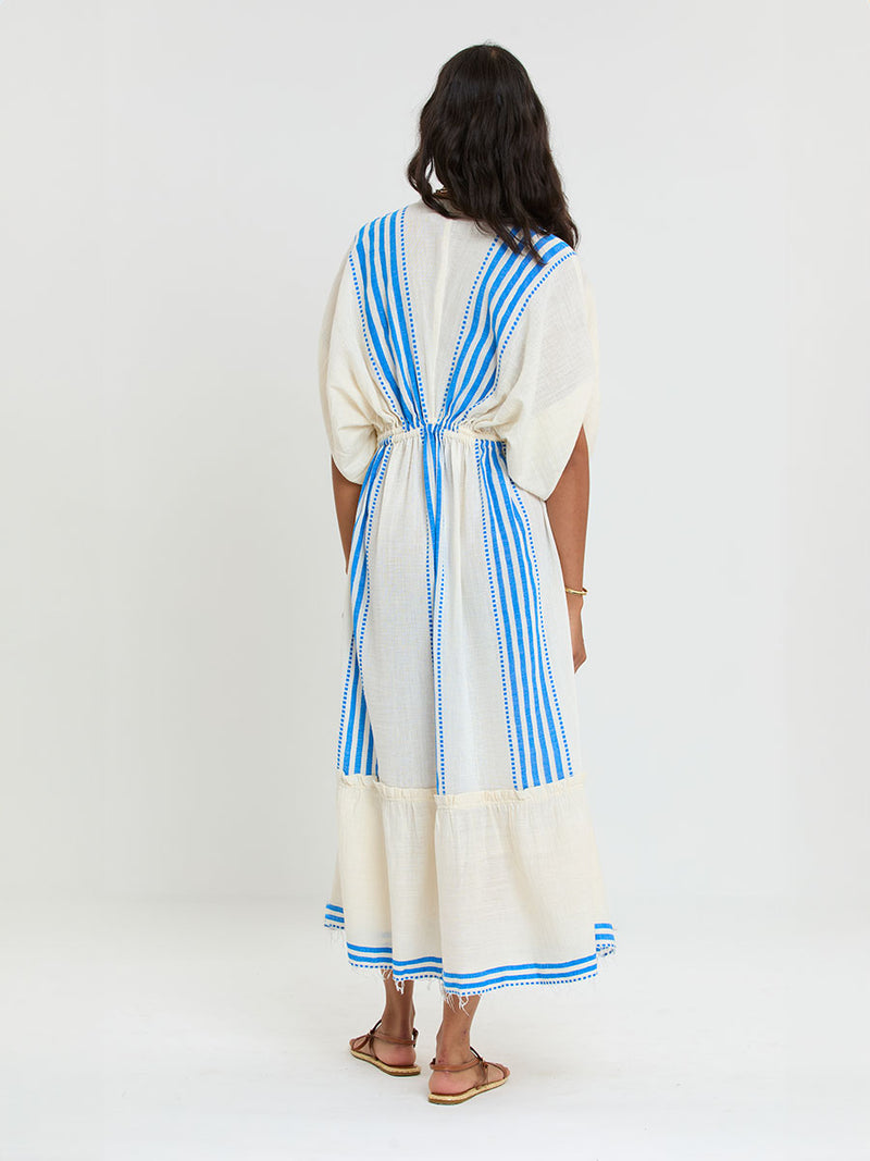 Back  of a Woman Standing Wearing lemlem LEILA Plunge Dress featuring striped pattern in blue color on cream background