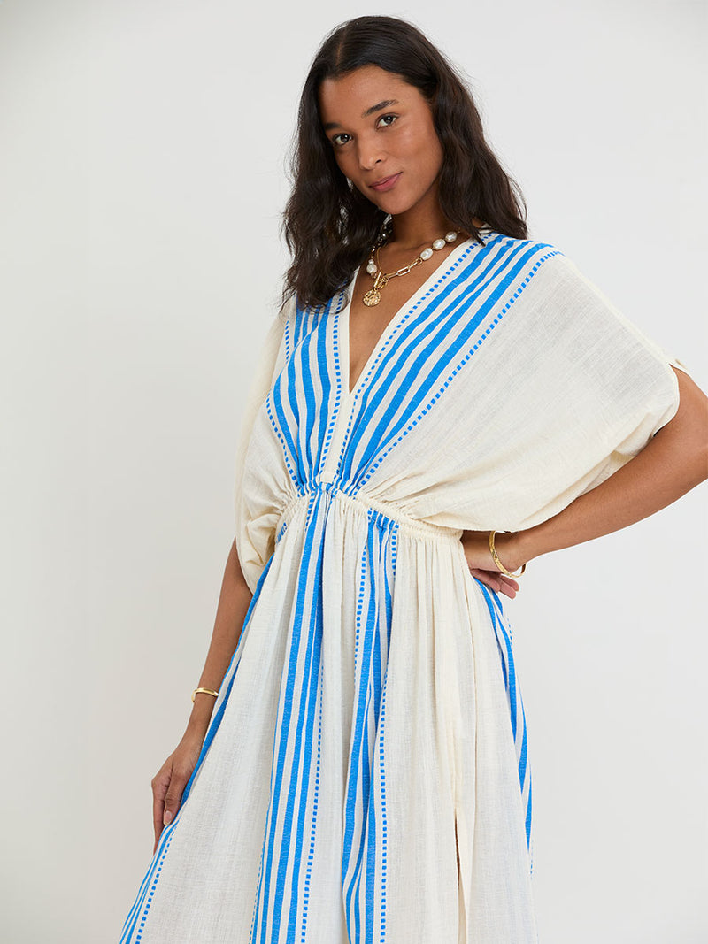 Woman Standing Wearing lemlem LEILA Plunge Dress featuring striped pattern in blue color on cream background