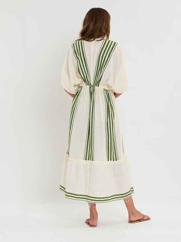 Back of a Woman standing wearing lemlem LEILA Plunge Dress featuring striped and dotted pattern in olive color on cream background