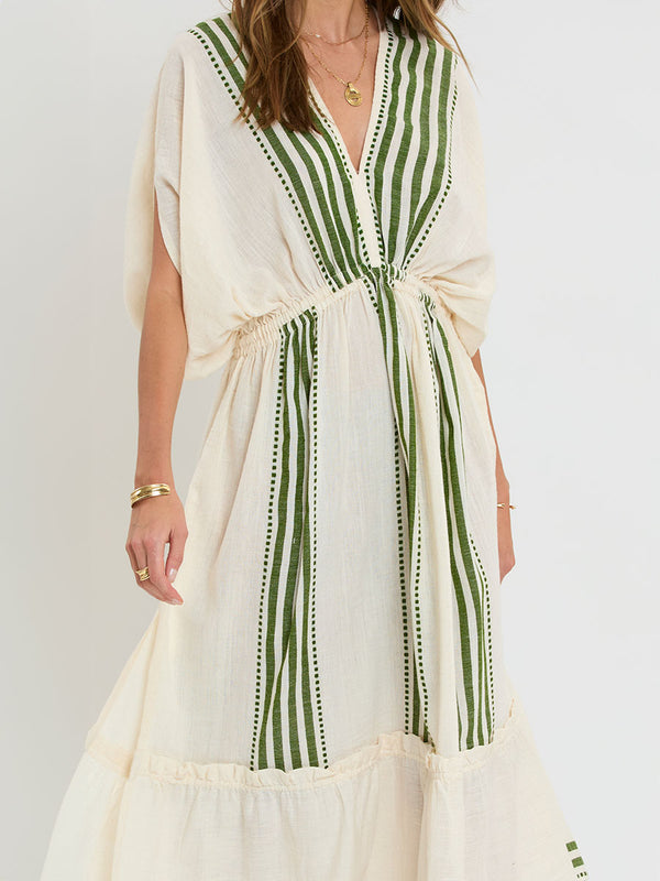 Close up on a Woman standing wearing lemlem LEILA Plunge Dress featuring striped and dotted pattern in olive color on cream background