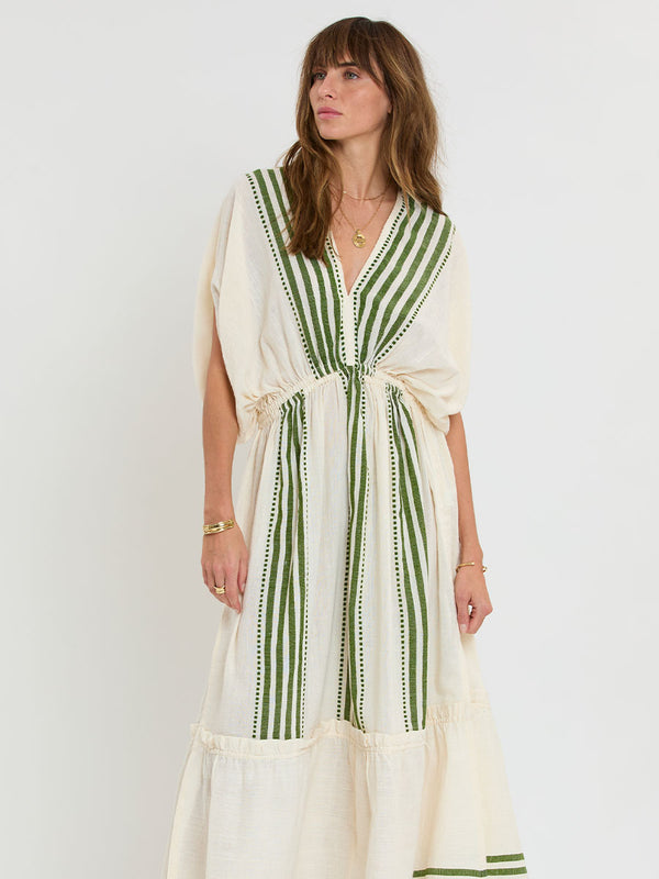 Woman standing wearing lemlem LEILA Plunge Dress featuring striped and dotted pattern in olive color on cream background