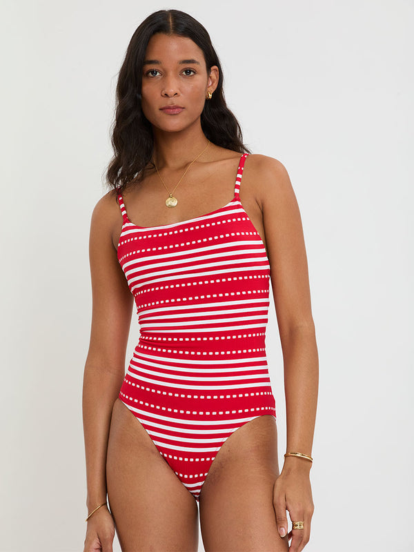 Woman wearing lemlem ELENE One Piece featuring a vanilla ground accented with vibrant red stripes and a dotted pattern. on a plain background