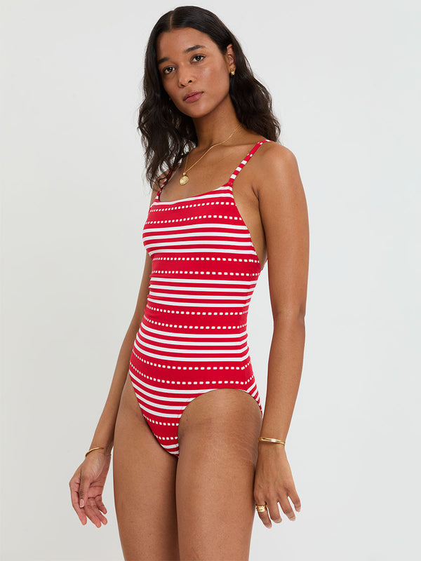 Woman wearing lemlem ELENE One Piece featuring a vanilla ground accented with vibrant red stripes and a dotted pattern. on a plain background