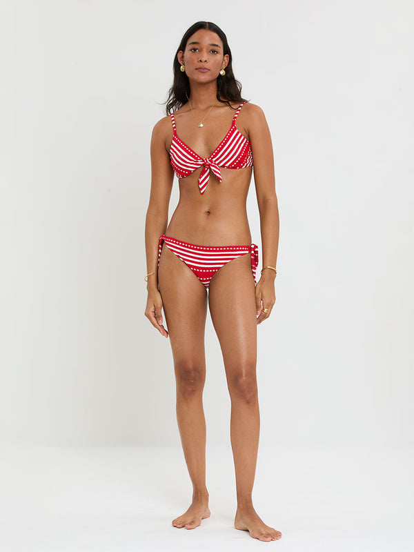 Woman wearing lemlem SARA Tie Front and LUCY Side Tie Bottom featuring a vanilla ground accented with vibrant red stripes and a dotted pattern. on a plain background