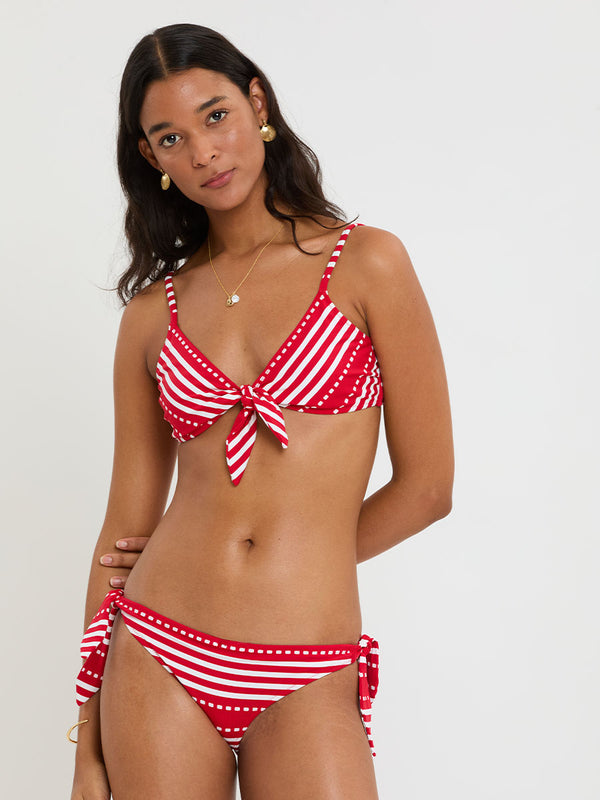 Woman wearing lemlem SARA Tie Front and LUCY Side Tie Bottom featuring a vanilla ground accented with vibrant red stripes and a dotted pattern. on a plain background