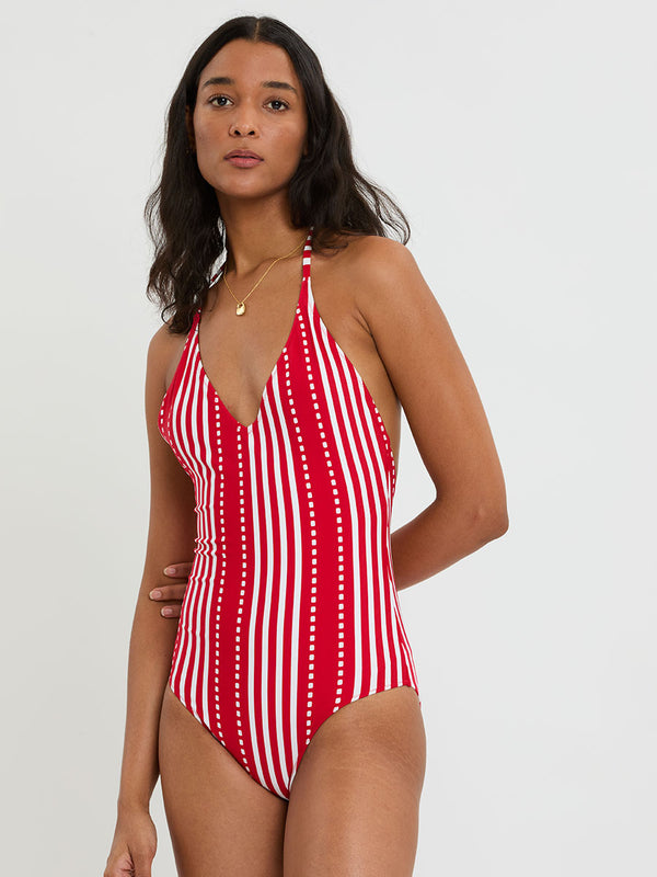 Woman wearing lemlem RETIRO One Piece featuring a vanilla ground accented with vibrant red stripes and a dotted pattern. on a plain background