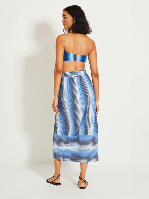 Back of a Woman Standing Wearing lemlem SALANA | Wrap Skirt featuring  stripe pattern that blends into a stunning ombré effect, with soft transitions between white, sky blue, mid blue, and deep navy.