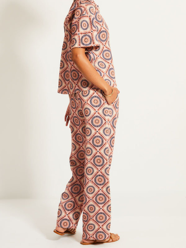 Side close up on a Woman Standing Wearing lemlem DIARRA | Pants  featuring a Yani Tibeb-inspired pattern in peach, rust, and orchid hues, accented with a bold citrus yellow pop and matching cabana shirt
