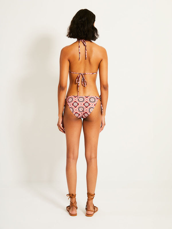 Back of a Woman Standing Wearing lemlem REKKA | String Bottom featuring a Yani Tibeb-inspired pattern in peach, rust, and orchid hues, accented with a bold citrus yellow pop and matching string bikini bottom

