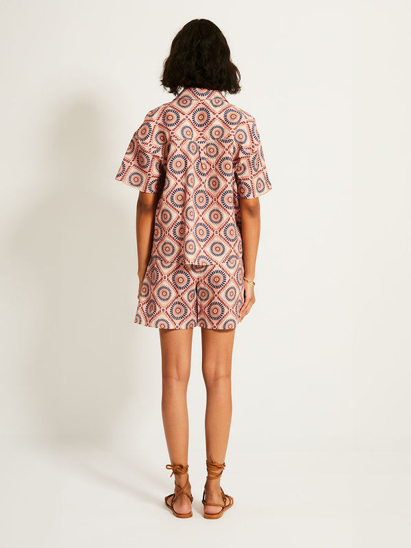 Back of a Woman Standing Wearing lemlem TUULI | Cabana Shirt  featuring a Yani Tibeb-inspired pattern in peach, rust, and orchid hues, accented with a bold citrus yellow pop.