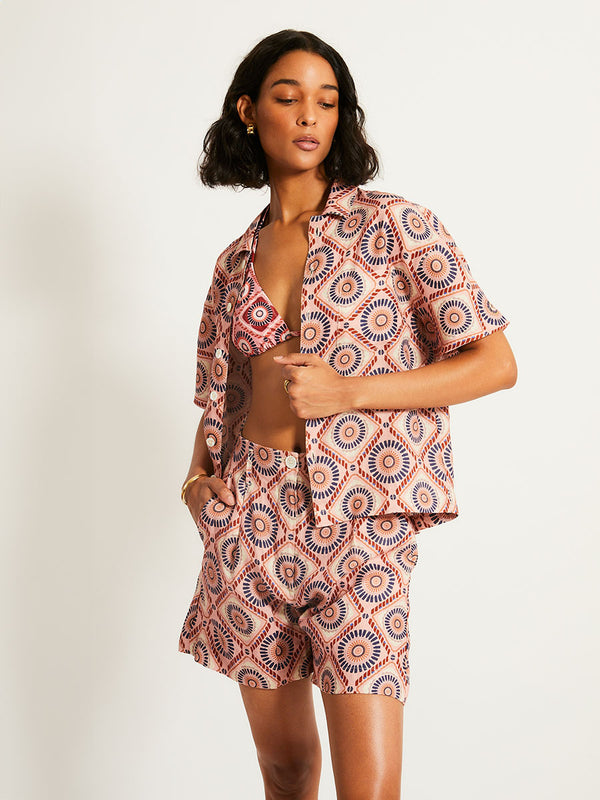 Woman Standing Wearing lemlem TUULI | Cabana Shirt  featuring a Yani Tibeb-inspired pattern in peach, rust, and orchid hues, accented with a bold citrus yellow pop.