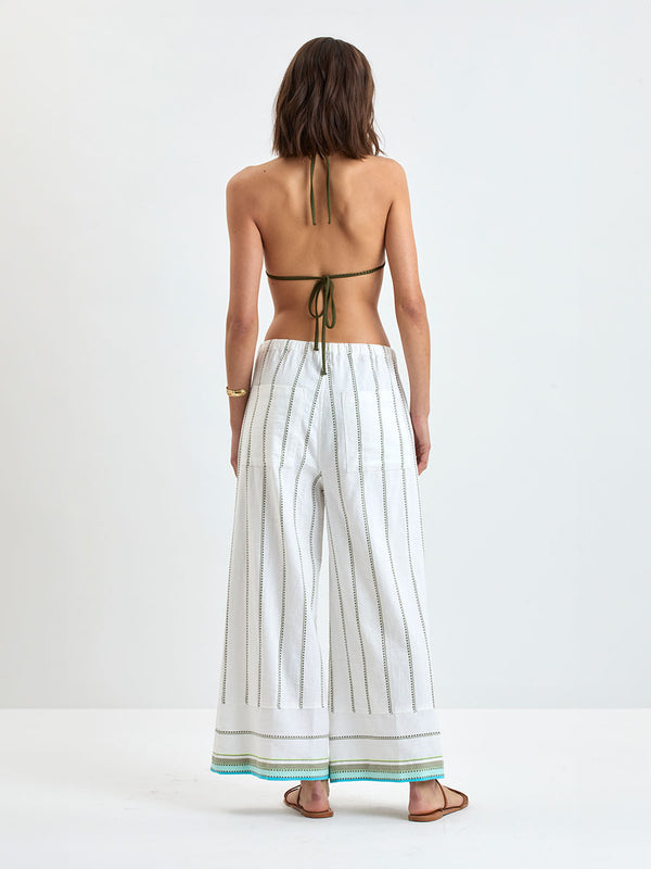 Back of a Woman wearing lemlem DESTA Pants  featuring a chic stripe pattern in aqua blue and sage tones, delineated by dark olive dots and accented with a splash of neon yellow on a cream background