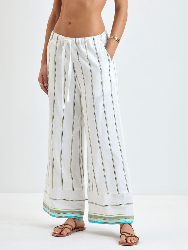 Close up on a Woman wearing lemlem DESTA Pants  featuring a chic stripe pattern in aqua blue and sage tones, delineated by dark olive dots and accented with a splash of neon yellow on a cream background