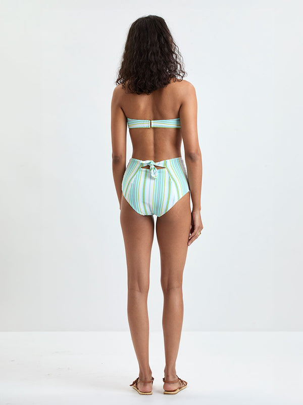 Back shot of a Woman wearing lemlem AVA Bandeau Top and ELSI High Waist Bottom featuring a chic stripe pattern in aqua blue and sage tones, delineated by dark olive dots and accented with a splash of neon yellow on a cream background